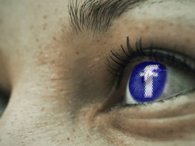 A person's eye with a Facebook logo as its iris