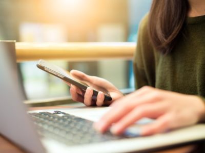 Woman connecting cellphone and laptop computer