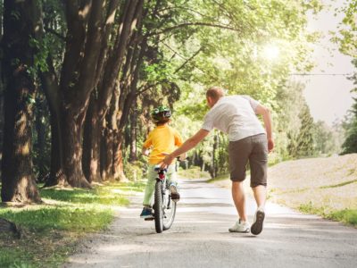 adult guy assisting a young boy riding a bicycle