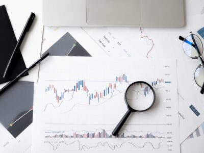 Flat lay of data visualization charts, graphs, and a magnifying glass on printed financial documents, illustrating data analysis in progress.